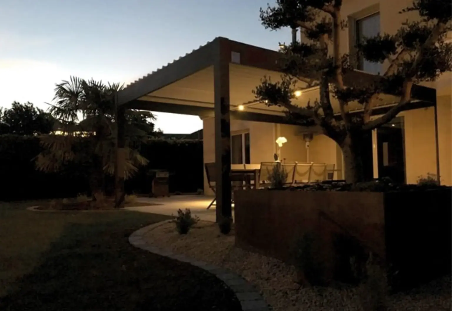 Pergola bioclimatique éclairée en soirée au-dessus d’une terrasse