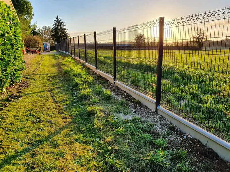 Longue clôture en panneaux rigides avec soubassement au coucher du soleil